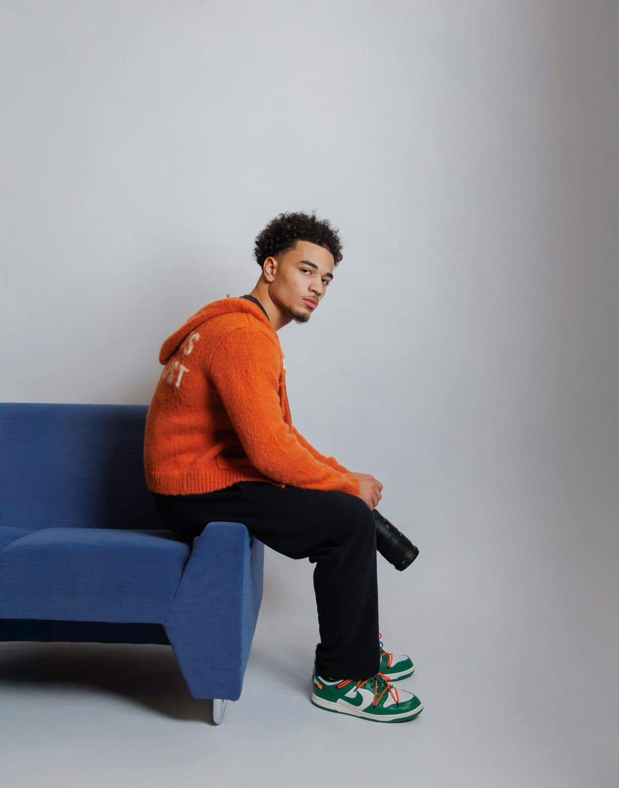 Jaedon Mast seated on a blue couch holding a camera lens